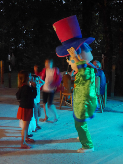 Niños bailan y juegan con una colorida mascota en un evento nocturno en Camping lac Aux Oiseaux, Occitanie.
