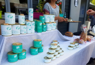 Market scene at Camping lac Aux Oiseaux in Occitanie, France, featuring canned food and tasting samples.