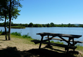 Træbord ved søen på Camping lac Aux Oiseaux, feriepark i Occitanie, Frankrig, med udsigt til vandet.
