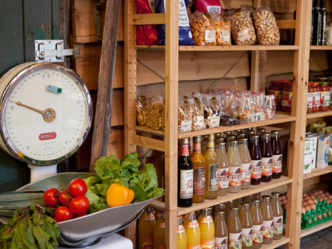 Tienda rural con verduras frescas, balanza antigua, bebidas embotelladas y snacks en Feather Down Het Wesselink.