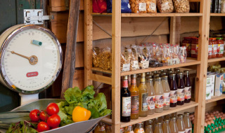 Tienda rural con verduras frescas, balanza antigua, bebidas embotelladas y snacks en Feather Down Het Wesselink.