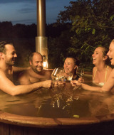 Cinco adultos disfrutan de una bañera de hidromasaje al aire libre con vino en Feather Down Het Wesselink en Salland.