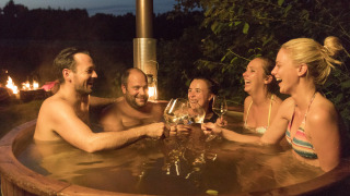 Cinq adultes savourent un bain à remous en bois avec du vin au Feather Down Het Wesselink à Salland.