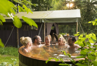 Fünf Freunde entspannen gemeinsam im Außenwhirlpool vor einem Zelt im Feather Down Het Wesselink, Salland.