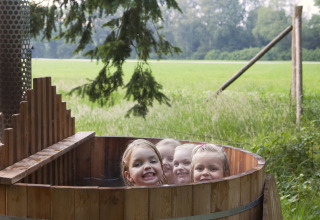 Quattro bambini sorridenti si rilassano in una vasca di legno all’aperto presso Feather Down Het Wesselink a Salland, Overijssel.