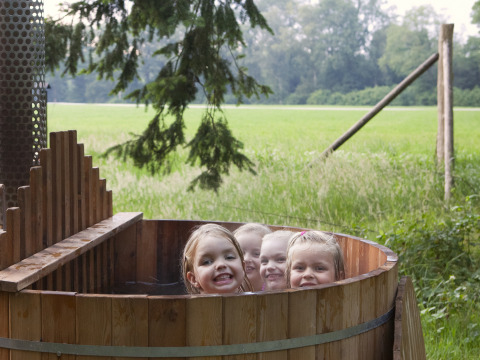 Vier Kinder baden in einer Holzbadewanne im Freien im Feather Down Het Wesselink in Salland, Overijssel, Niederlande.