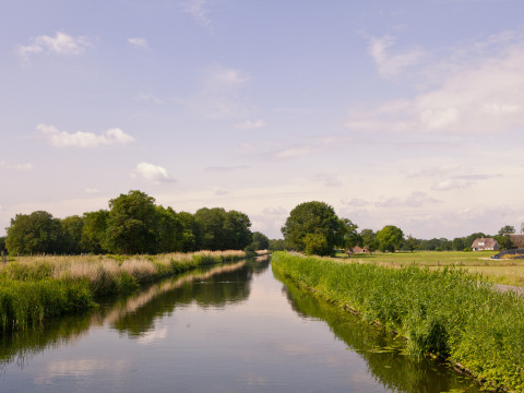 Paisaje de canal en Feather Down Het Wesselink en Salland, Overijssel, Países Bajos, con casas rurales al fondo.