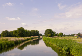 Tranquil canal scene at Feather Down Het Wesselink in Salland, Overijssel, Netherlands, with farmhouses nearby.