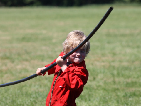 Een kind in een rode overall speelt buiten met een zwarte slang op het veld bij Feather Down Het Wesselink, Overijssel.