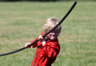 Un enfant en combinaison rouge joue avec un tuyau noir dans un champ à Feather Down Het Wesselink, Overijssel.