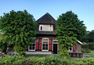 Casa tradizionale olandese con tetto di paglia e persiane rosse, circondata da alberi verdi in Overijssel.