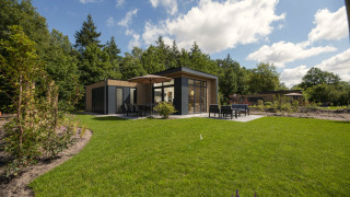 Modernes Lodge mit großer Terrasse, Sitzmöbeln und Sonnenschirm umgeben von Garten und grüner Natur.