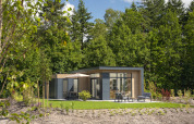 Moderne Lodge mit großen Fenstern und Terrasse im Grünen, umgeben von Bäumen und gemütlichen Gartenmöbeln.