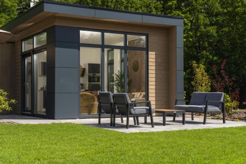 Moderne lodge met grote ramen, terras, buitenzitplaats en netjes onderhouden grasveld ervoor.