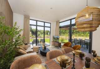 Lyst og moderne lodge-interiør med spisebord, siddeområde, store vinduer og udsigt til have.
