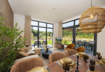 Licht en modern lodge-interieur met eettafel, zithoek, grote ramen en uitzicht op de tuin buiten.