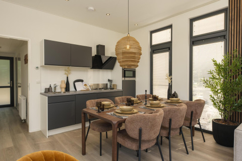 Modern lodge interior with kitchen, dining table set for six, large windows, and plenty of natural light.