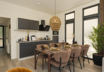 Modern lodge interior with kitchen, dining table set for six, large windows, and plenty of natural light.