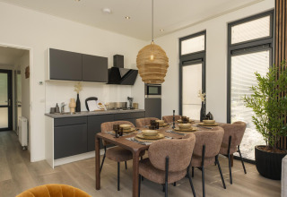 Interno di un lodge moderno con cucina, tavolo da pranzo per sei, grandi finestre e luce naturale.