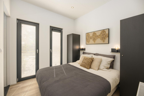 Bright bedroom in a lodge featuring a double bed, two wardrobes, soft lighting, and modern minimalist decor.