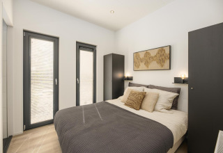 Bright bedroom in a lodge featuring a double bed, two wardrobes, soft lighting, and modern minimalist decor.