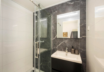 Bagno moderno in un lodge con doccia in vetro, lavabo scuro, grande specchio e piastrelle marmorizzate.