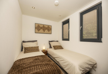 Chambre moderne dans un lodge avec deux lits simples, coussins marron, fenêtres et lumière tamisée.