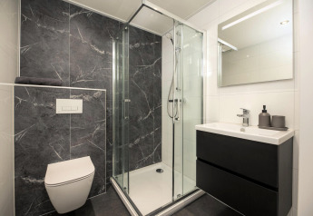 Modernes Badezimmer in einer Lodge mit dunklen Fliesen, Duschkabine, Wandtoilette und Waschtisch.