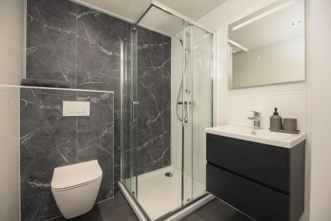 Moderne lodgebadkamer met marmerlook zwarte tegels, glazen douche, zwevend toilet en wastafel.