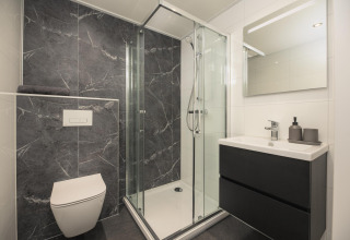 Modern lodgebadkamer met marmeren zwarte tegels, glazen douchecabine, hangtoilet en wastafelmeubel.