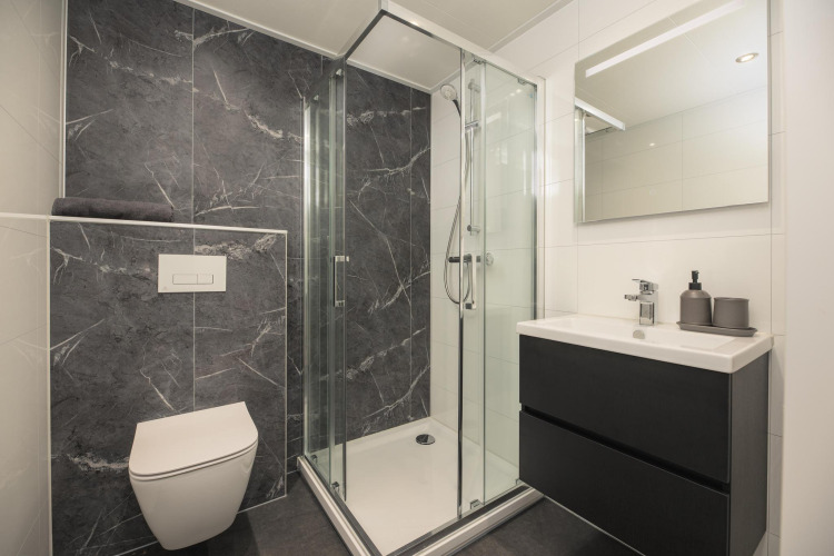 Baño moderno en lodge con azulejos negros, inodoro suspendido, ducha de cristal y lavabo minimalista.