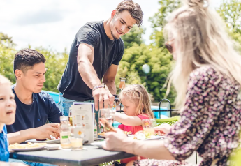 Family enjoys an outdoor meal at a glamping site, smiling together in sunny weather and nature.