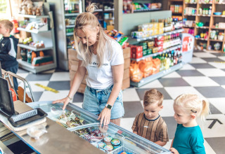 Una madre y dos niños eligen helado de un congelador en la tienda de una cabaña llena de comestibles.
