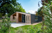 Casa de madera moderna en Panorama Cottage, Kaatsheuvel, Países Bajos, rodeada de vegetación y jardín.