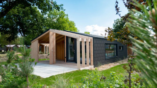 Casa de madera moderna en Panorama Cottage, Kaatsheuvel, Países Bajos, rodeada de vegetación y jardín.