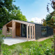 Casa de madera moderna en Panorama Cottage, Kaatsheuvel, Países Bajos, rodeada de vegetación y jardín.