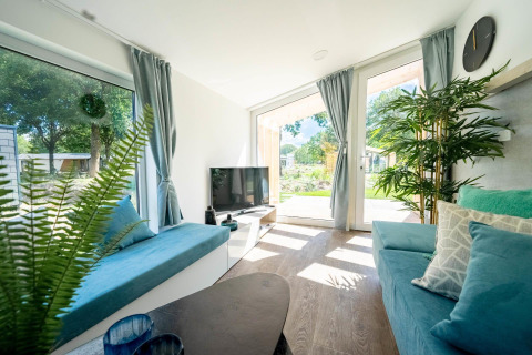 Salon lumineux du Panorama Cottage à Kaatsheuvel, Pays-Bas, avec de grandes fenêtres et une décoration bleue.