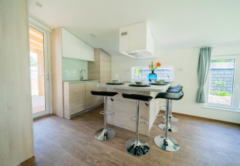 Moderne spiseplads og køkken i Panorama Cottage, Kaatsheuvel, Holland, med lyse træmøbler og vinduer.
