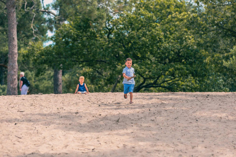 Zwei Kinder spielen im Sand vor Bäumen bei Panorama Cottage in Kaatsheuvel, Niederlande.