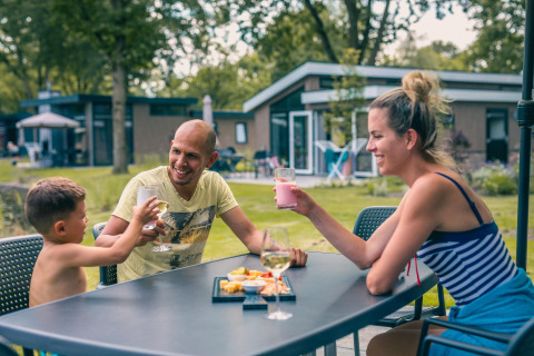 Familie genießt Getränke und Snacks im Freien vor der Panorama Cottage Lodge in Kaatsheuvel, Niederlande.