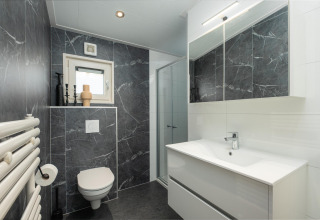 Moderne badkamer met zwart marmer, witte elementen en glazen douche in Loevestein Deluxe op Veluwepark.