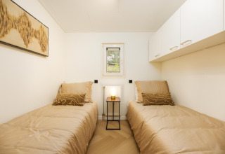 Habitación luminosa en lodge con dos camas individuales, ropa de cama beige, arte mural y una lámpara de mesa.