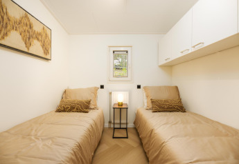 Habitación luminosa en lodge con dos camas individuales, ropa de cama beige, arte mural y una lámpara de mesa.