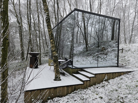 Et spejlkubeformet tiny house, ÖÖD Suite, står på en snedækket terrasse i en skov ved Wilsumer Berge.