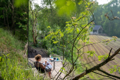 Vrouw ontspant op terras bij ÖÖD Suite in Wilsumer Berge, Duitsland, omgeven door groene natuur.