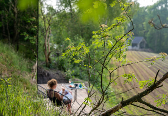 Vrouw ontspant op terras bij ÖÖD Suite in Wilsumer Berge, Duitsland, omgeven door groene natuur.