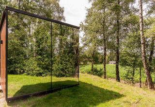 Spiegelende glazen gevel van de ÖÖD Suite tiny house in Wilsumer Berge, Duitsland, te midden van groen.