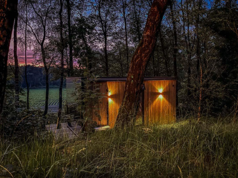 Tiny house ÖÖD Suite ved Wilsumer Berge i Tyskland, omgivet af skov, set i skumringen med lys tændt.