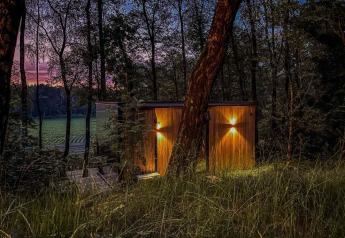 Tiny house ÖÖD Suite à Wilsumer Berge en Allemagne, éclairée en pleine forêt au crépuscule avec lumières allumées.