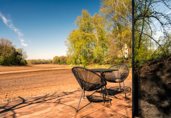 Outdoor terrace at ÖÖD Suite Wilsumer Berge, Germany, featuring two chairs, a table, and scenic field view.